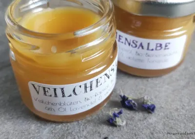 Gläser mit Veilchensalbe und Hagebuttensalbe mit getrockneten Blüten